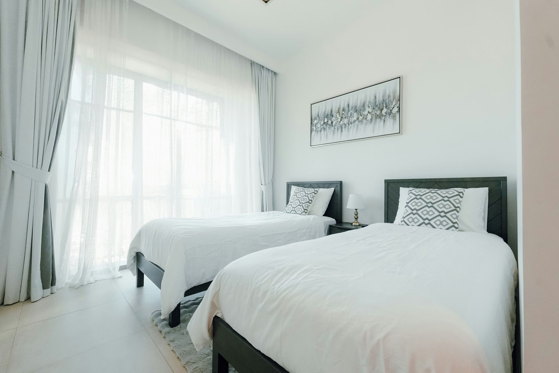 Two beds in a bright, modern bedroom with large windows.